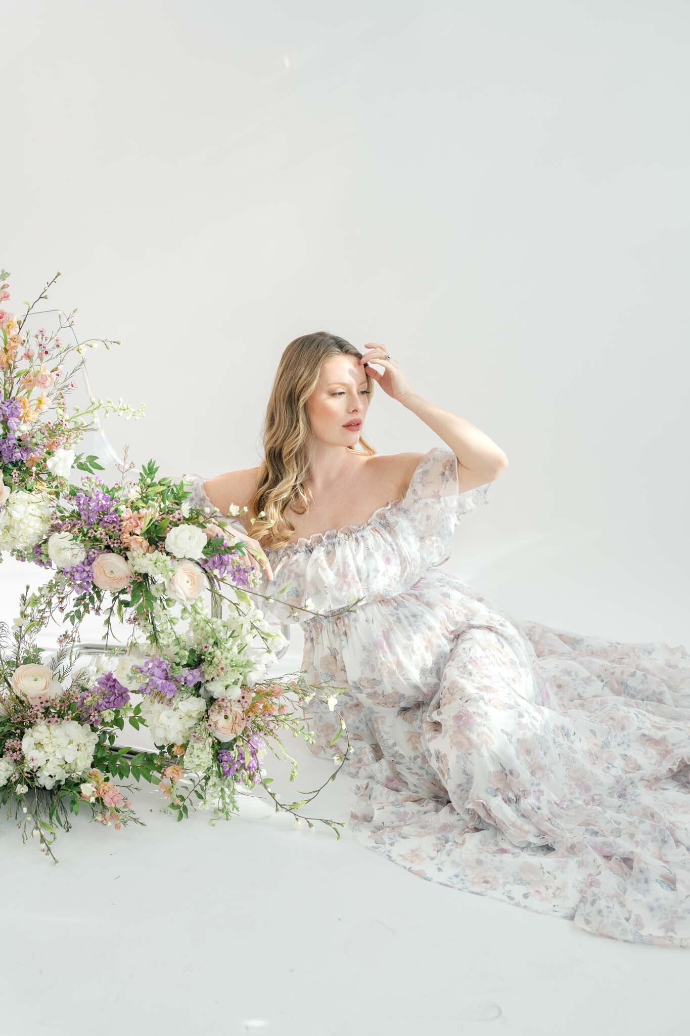 expecting mother sitting beside a chair full of flowers in glowy light taken by Salt Lake City Utah maternity photographer Kamee Valdez Photo