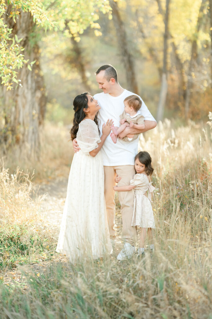 Fall family photos in Snow Basin featuring a family of four embracing together beneath towering trees with beautiful golden autumn colors.