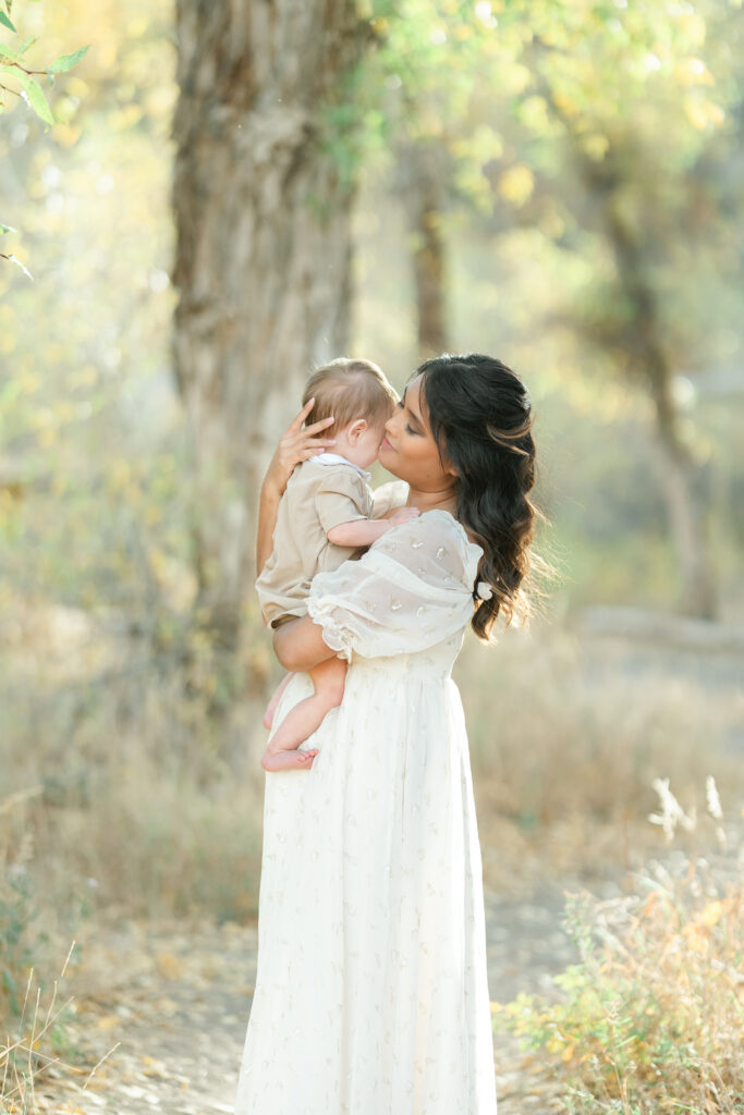 Snow Basin fall family photos capturing a tender moment as a mother kisses her baby while surrounded by soft golden fall foliage.