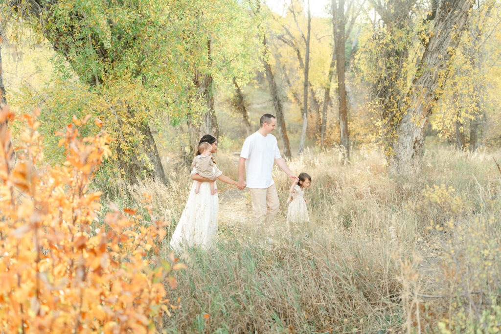Snowbasin fall family photos by Kamee Valdez Photo featuring a young family walking hand in hand through golden autumn trees in Snowbasin, Utah during a warm sunset portrait session.