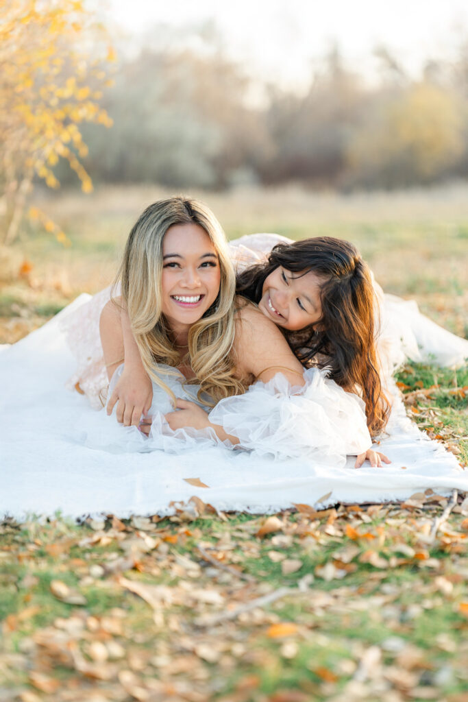 Mother and daughter cuddling outdoors beneath golden autumn trees during fall activities in Utah taken by Kamee Valdez Photo