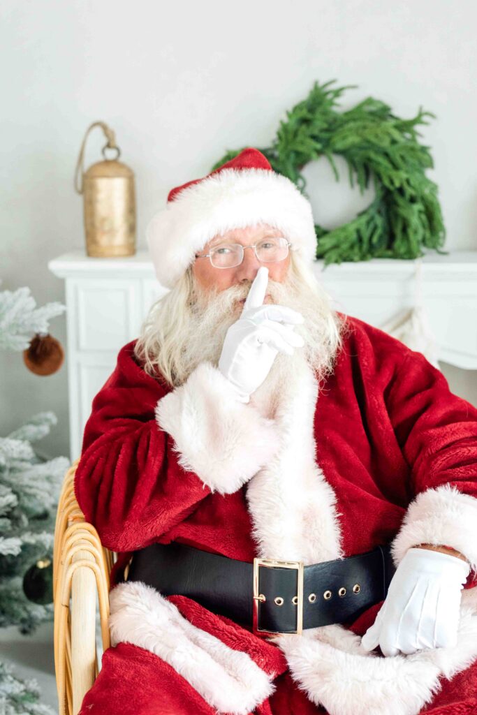 Santa holding a finger to his lips during Utah Santa photos in a bright, timeless Christmas studio by Kamee Valdez Photo.