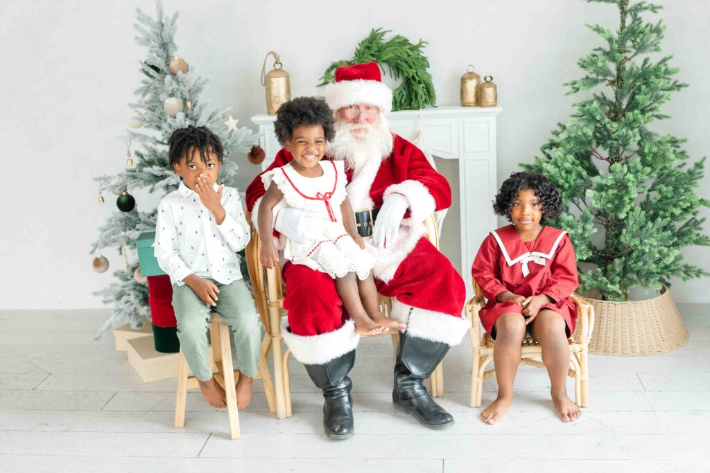 Three children posing with Santa for Utah Santa photos in a timeless Christmas studio by Kamee Valdez Photo.