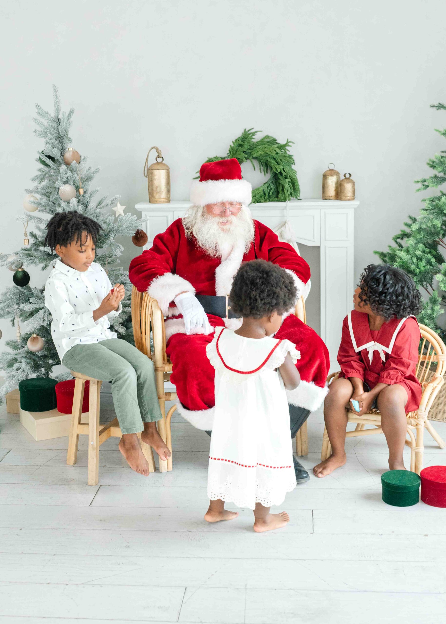 Three children visiting Santa during Utah Santa photos surrounded by Christmas trees and holiday decor by Kamee Valdez Photo.
