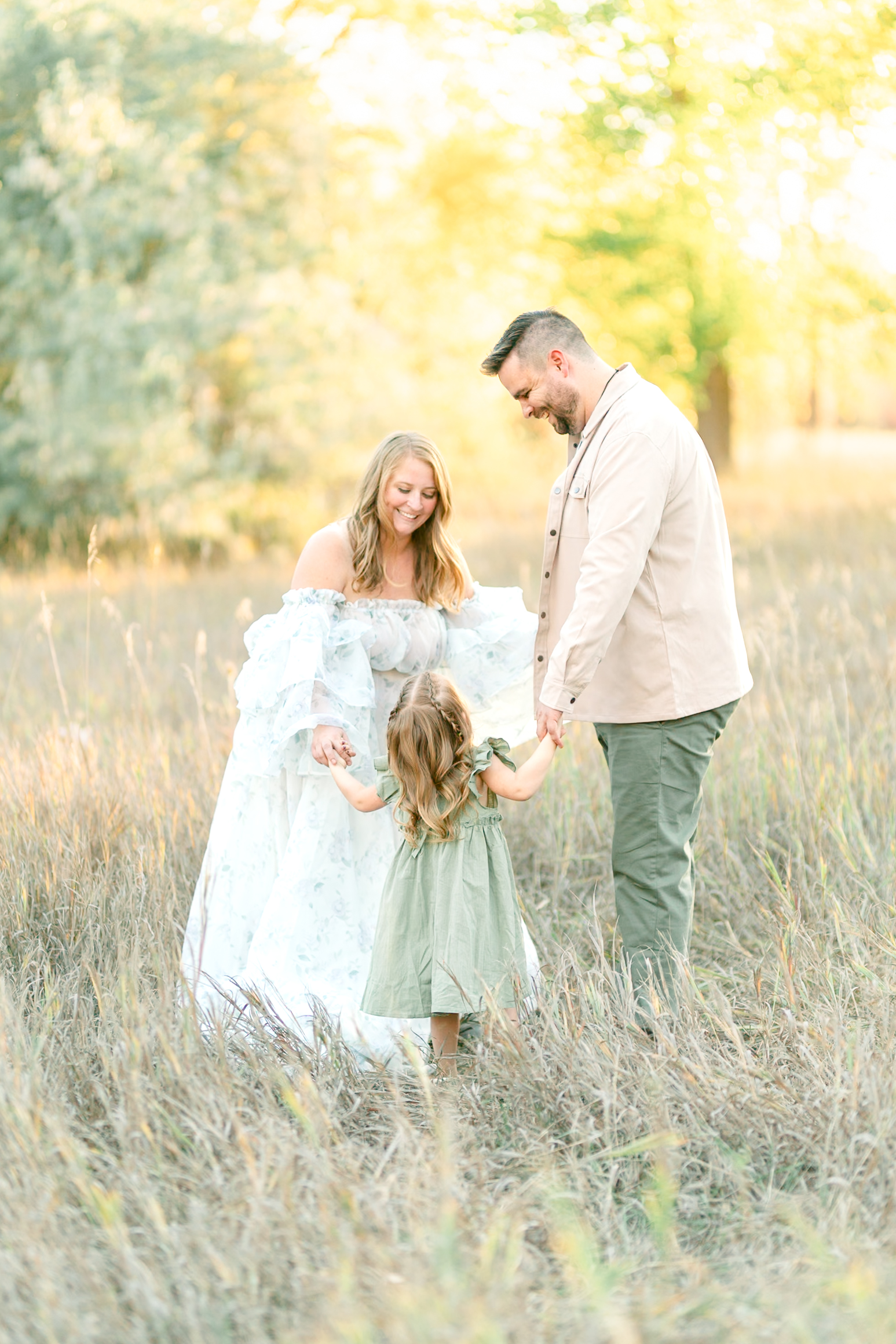 Family standing together on a tree-lined pathway at Kayscreek Parkway in Utah, surrounded by golden autumn leaves. Warm sunlight filters through the branches, highlighting the family’s smiles and the vibrant fall colors.