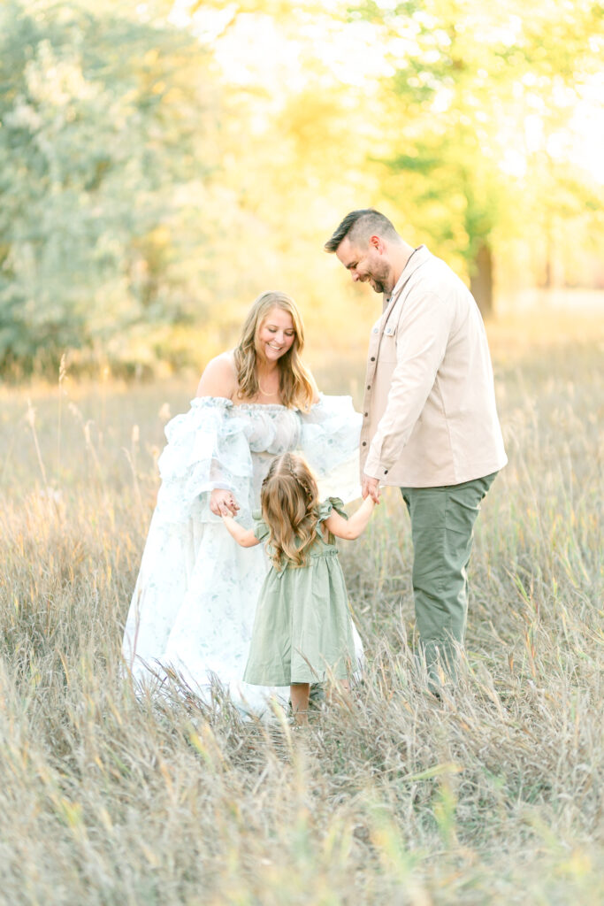 Family standing together on a tree-lined pathway at Kayscreek Parkway in Utah, surrounded by golden autumn leaves. Warm sunlight filters through the branches, highlighting the family’s smiles and the vibrant fall colors.